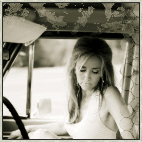 A vintage photograph captures a woman sitting in a car, gazing down with a contemplative expression. The sepia tones and delicate textures evoke a sense of nostalgia and introspection. Her long hair cascades around her face, framing her features. The artful composition and the interplay of light and shadow create a timeless and evocative image.